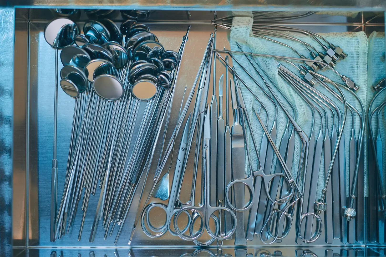 Array of stainless steel medical instruments including scissors, scalpels, and mirrors neatly arranged for surgical use.